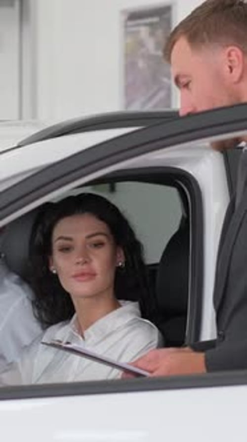 Vertical Video a Brunette Woman Sits Behind the Wheel of a New Car in a Car Showroom