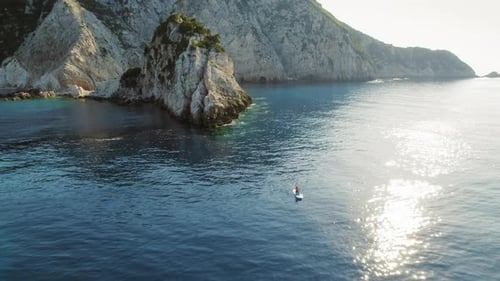 Person kayaking in a calm bay near dramatic limestone cliffs on Kefalonia island in Greece