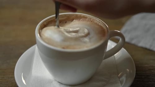 Stirring Cappuccino in White Mug with Spoon