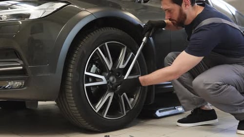 Mechanic Tightening Wheel Nuts with Wrench in Auto Repair Shop