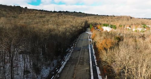 Car vehicle driving on empty road by winter leafless forest, sunny, aerial shot