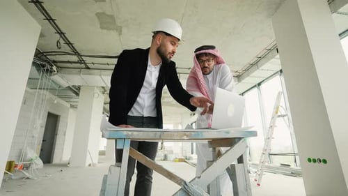 Architect and Arab Investor Discussing Building Plans on Construction Site