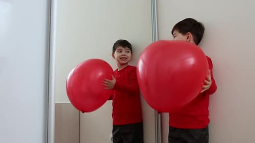 Two Young Children Play with Big Red Balloons