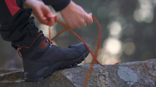 Man stepping on a rock and tying his shoelaces. Outdoors and hiking