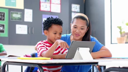 In school, teacher and student using tablet together in classroom, smiling