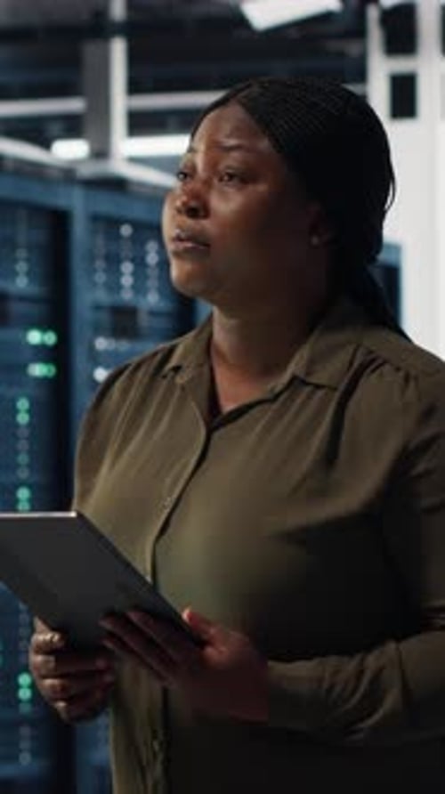 Vertical Video Engineer with Tablet Walks Through Data Center Server Rows
