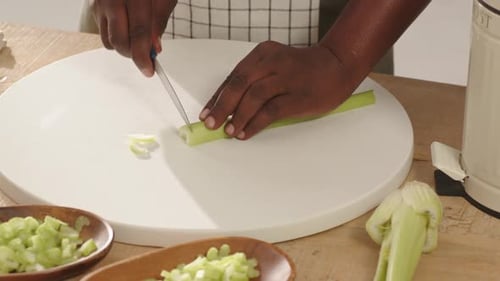 Celery stalks are being sliced on round cutting board with blue knife, diced piles forming