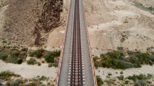 aerial forward slow drone shot of an empty train rail bridge, revealing the desert in day light.