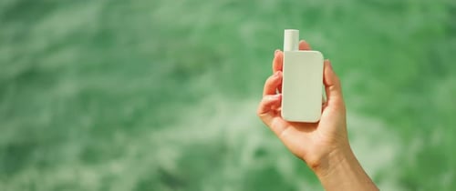 Female hand holding cosmetic product sunscreen SPF cream against ocean waves sea water background. C