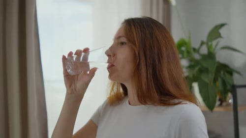 A Beautiful Young Adult Woman is Drinking Clean Water From a Transparent Glass