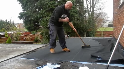 Labourer brushing air bubbles from rubber sheet fixing damaged flat garage roofing