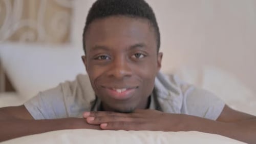 Jeune homme africain faisant les pouces levés en position couchée sur le ventre dans son lit
