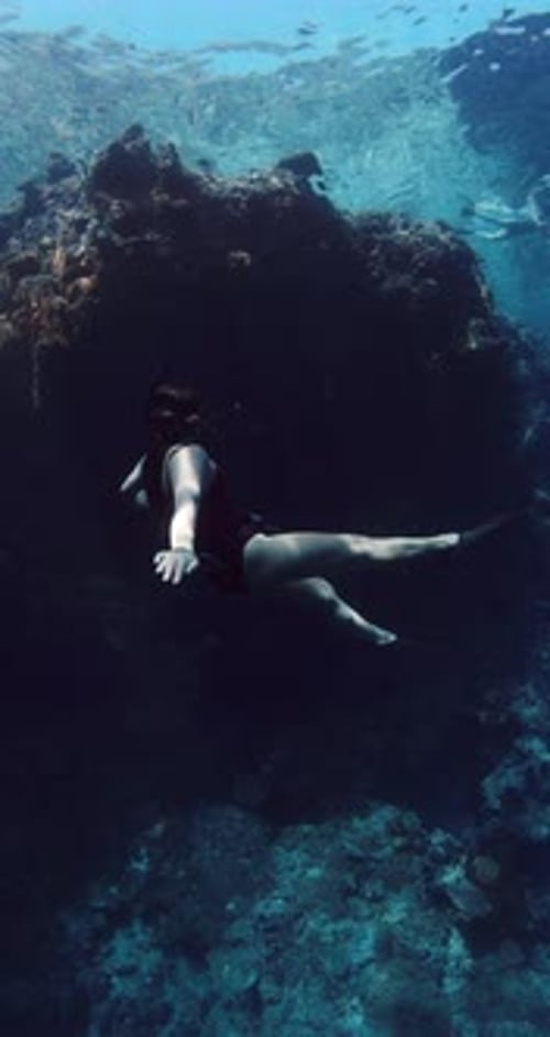Freediver Swims in Ocean with Sun Rays Woman Freediving in Blue Sea Near Rocks and Coral Reef