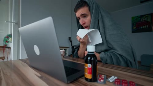 Man Wrapped in Blanket Sneezes Covering Mouth with Napkin