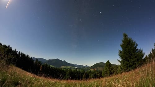 Zeitraffer des Sternenhimmels mit Mond über Bergtal und Waldhügeln in malerischer Landschaft