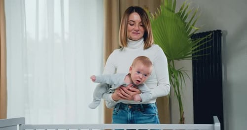 Young Woman Holding Adorable Baby Near Crib