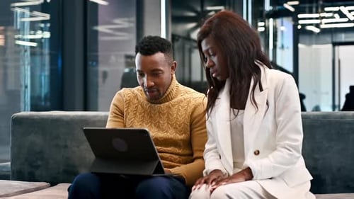 Black male and female workers in an office discussing and working using a tablet. Slow motion