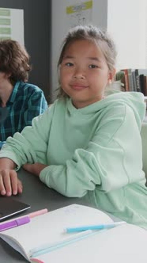 Portrait of Asian Girl Sitting at Desk in Modern School Classroom