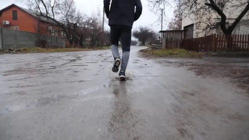 Beine eines jungen Sportlers, der an einem Regentag auf einem ländlichen Pfad läuft Männliche Füße eines sportlichen Läufers beim Joggen