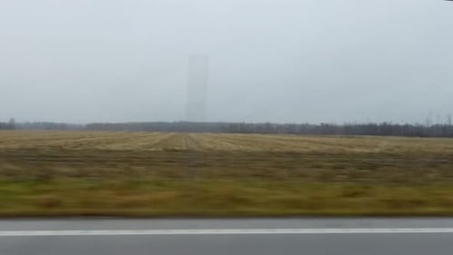 Wide shot of an expansive rural field under an overcast sky, offering a serene view of the countrysi