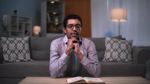 Religion Schwarzer Mann liest Bibel und betet mit verschränkten Händen im Zimmer, bevor er schlafen geht
