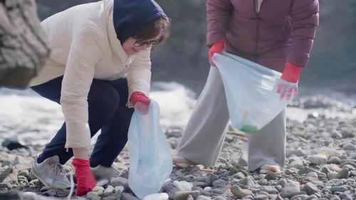 Two Young Women Collecting Plastic Trash and Other Garbage on the Beach Cleaning Up Polluted