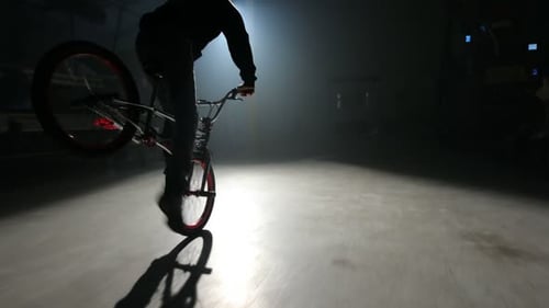 Young bmx rider performing stunts in a dark urban warehouse environment