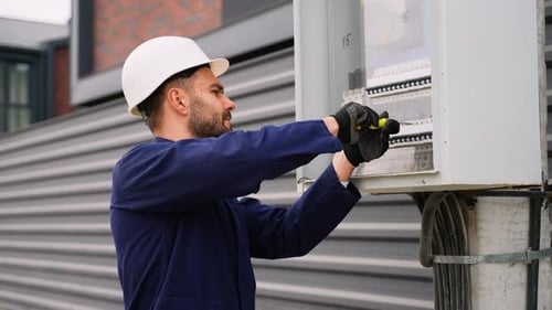 Man Adjusts Fuse in Junction Box on Building Exterior