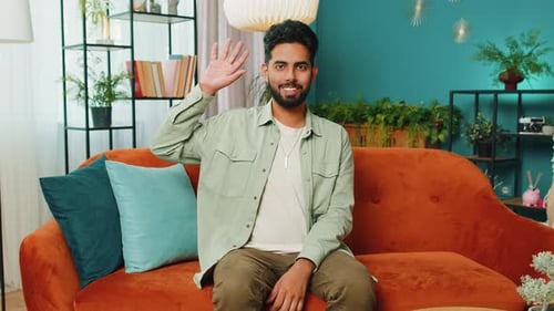 Smiling Man Waving and Talking on Couch