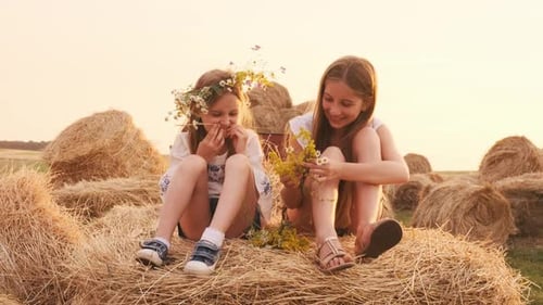 Girls with Flowers Sitting on Hay Bale at Sunset
