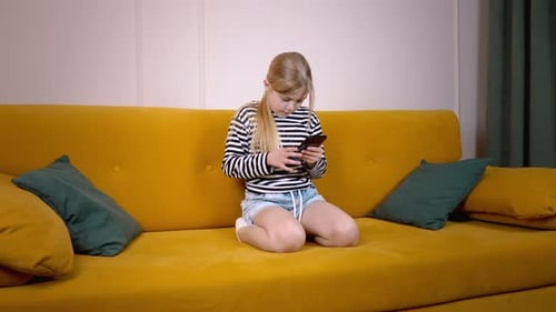Girl Using Smartphone on Yellow Sofa at Home