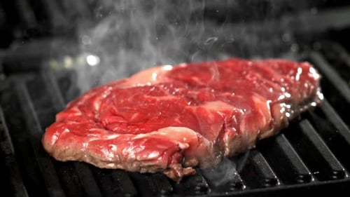 Raw Steak Cooking on a Black Grill