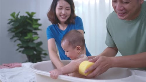 Parents Bathing Adorable Baby in Home Bathtub