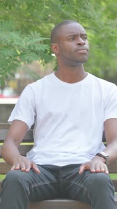 African American Man Checking Time while Sitting on Bench in Park, Vertical Video