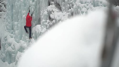 Ice climber climbing on frozen waterfall in cold white winter mountain landscape