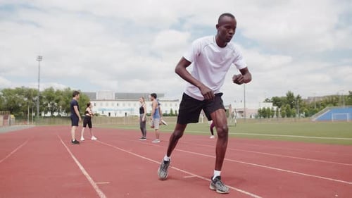 A Black Guy in Sportswear Gets Into Position at the Stadium Warms Up His Body and Muscles Before