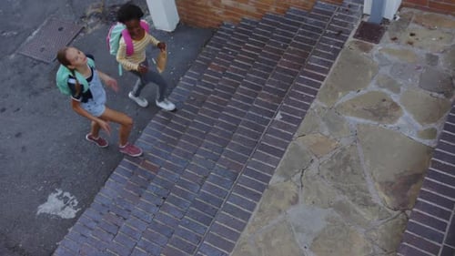 Walking up stairs, two girls with backpacks talking after school