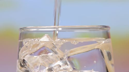Close Up Of Drinking Water Being Poured Into A Glass With Ice Cubes On Pink Nature Screen Background