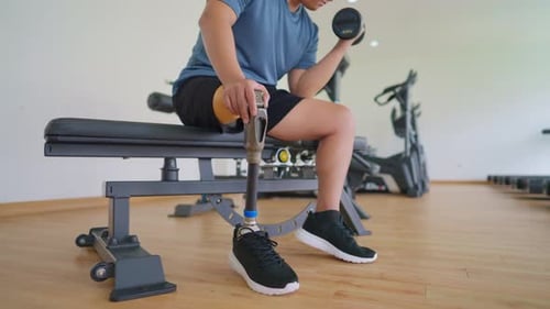 Asian young man with a prosthetic leg lifts a dumbbell at the gym.