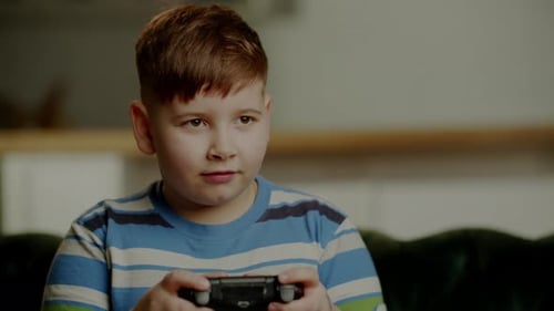 Konzentriertes Kind im gestreiften T-Shirt spielt Video, Junge mit Gamecontroller, drückt Glück aus