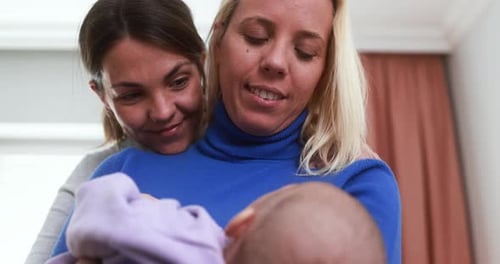 Two Women Cradling Smiling at Infant Together Indoors