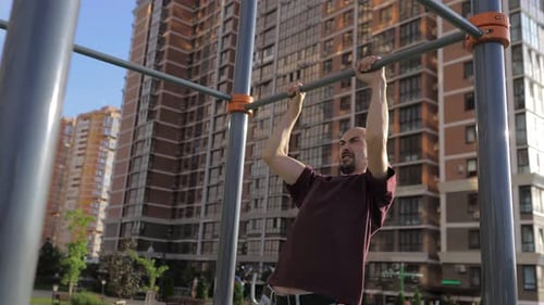 A Young Man with Thin Skin Body is Pulling Up on a Street Sports Ground in a Beautiful City Park in