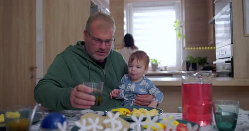 Father feeds baby at table in home kitchen