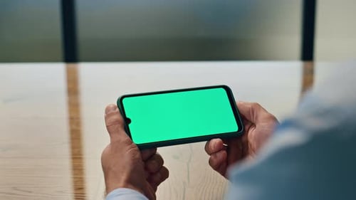 Man Holds Smartphone with Green Screen in Home