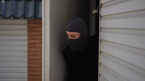 Une jeune cambrioleuse masquée se faufile par l'entrée du garage pour entrer dans la maison