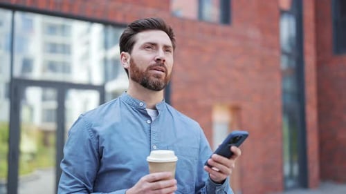 Businessman Enjoys Coffee and Uses Smartphone Near Office Building