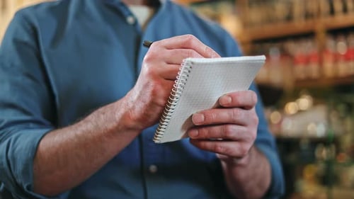 Close Up of Male Food Service Worker Writing Order on Paper Notebook Indoors