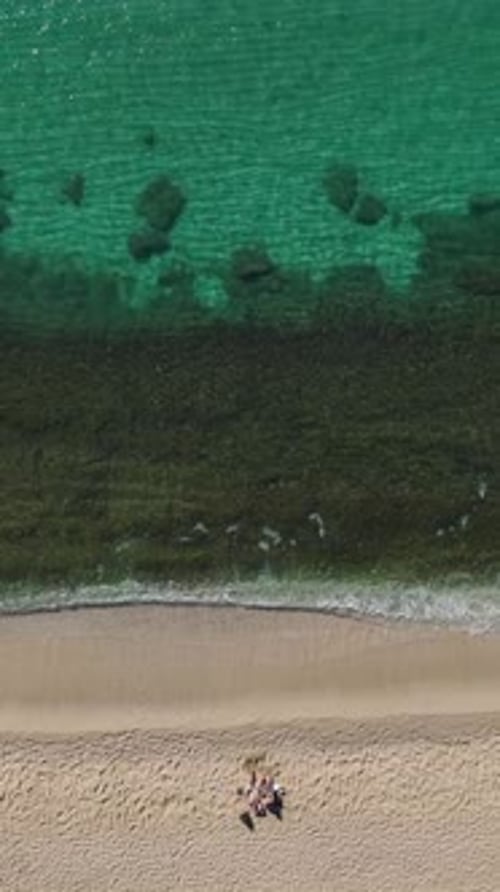 Vertikales Video: Szenischer Blick auf einen Strand mit klarem Wasser und strahlend blauem Himmel, aufgenommen von oben