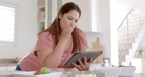 Woman Reads Tablet while Cooking at Kitchen Counter