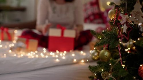 Woman Unwrapping Christmas Gift by Decorated Christmas Tree